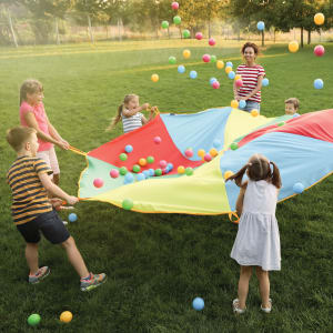 Children playing outdoors with a colorful parachute and bouncing balls on a grassy field