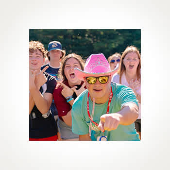 A group of energetic young people, with one wearing a pink cowboy hat and sunglasses