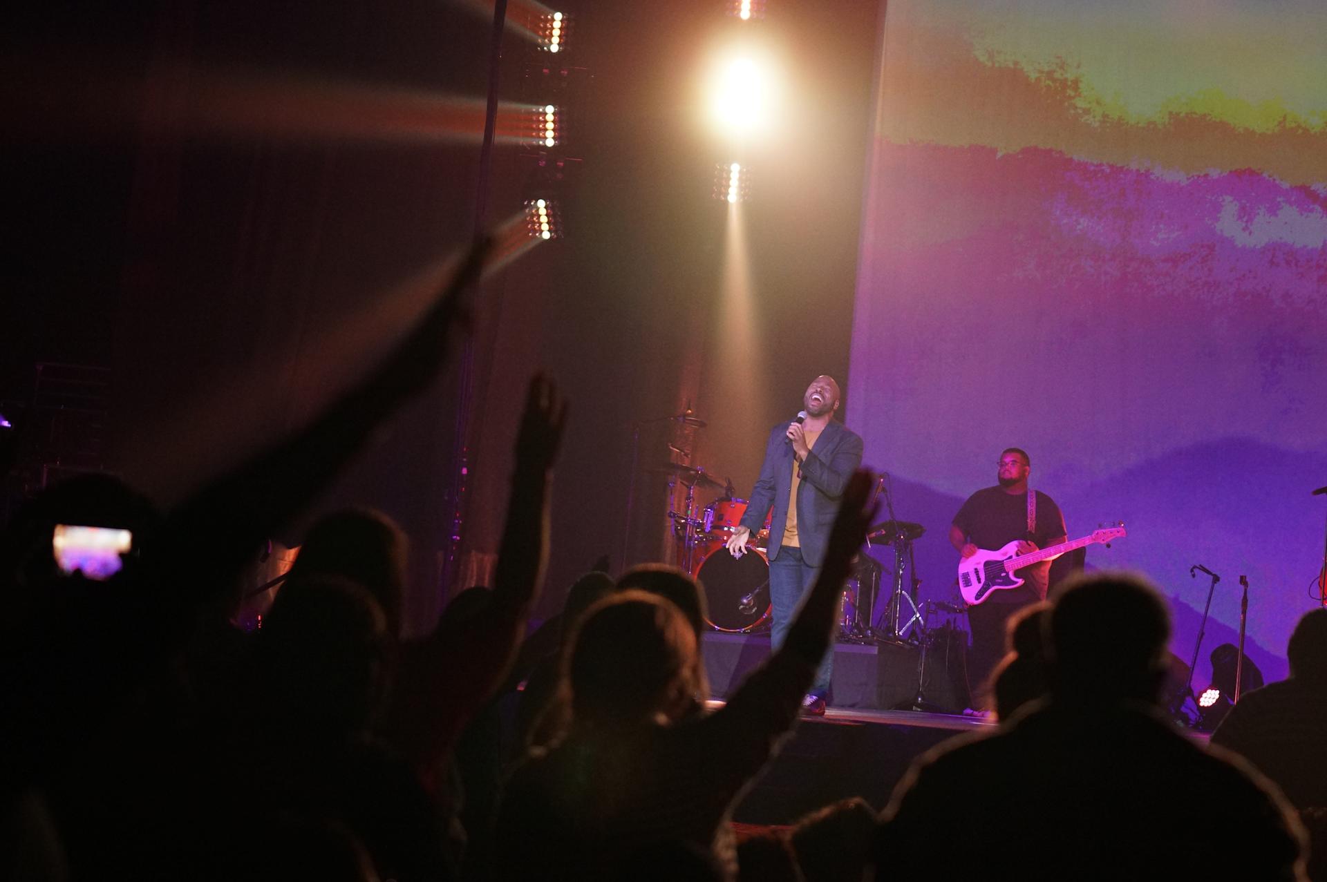 A worship leader on stage with hands raised in worship in the audience