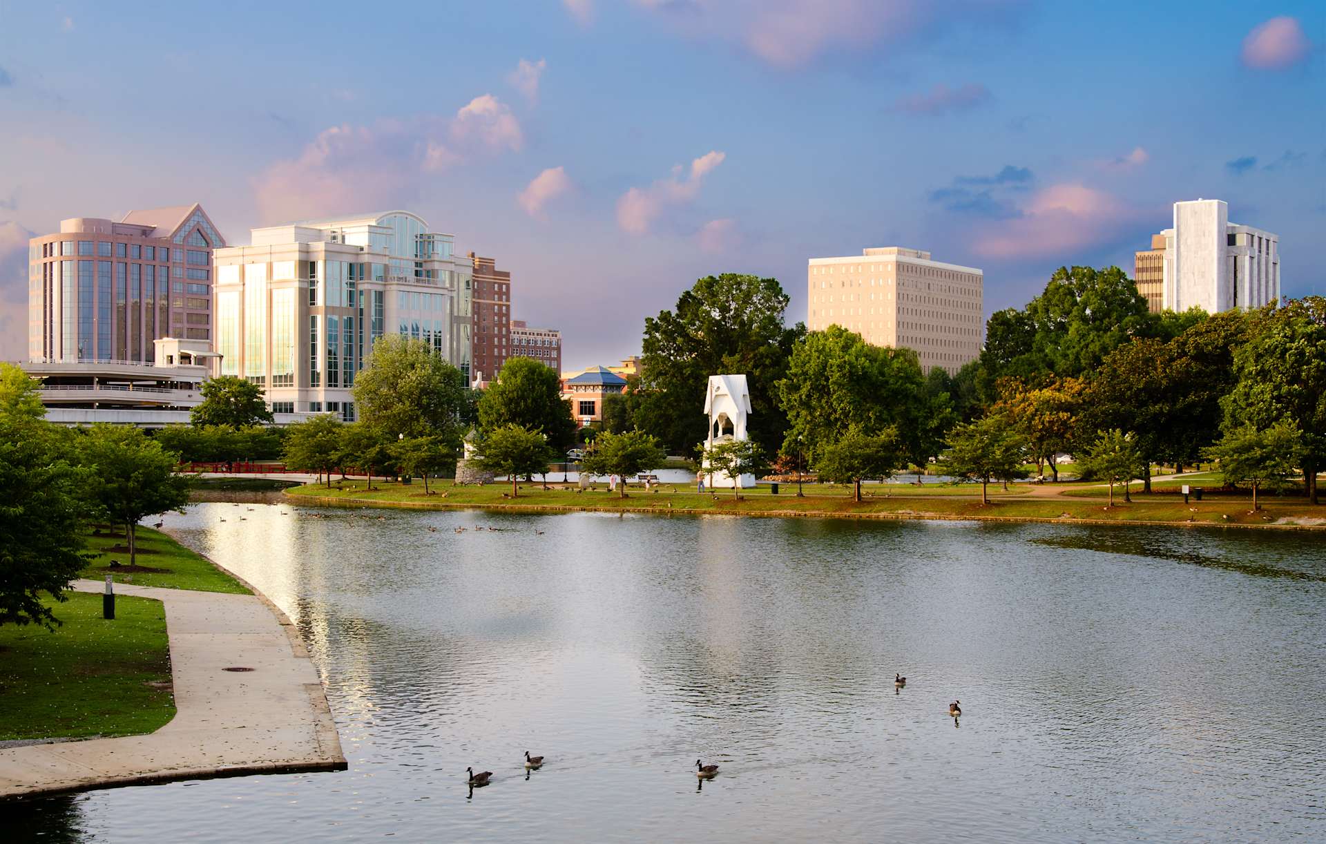 Tranquil lake surrounded by greenery and downtown buildings in Huntsville, Alabama, with a few ducks swimming in the water