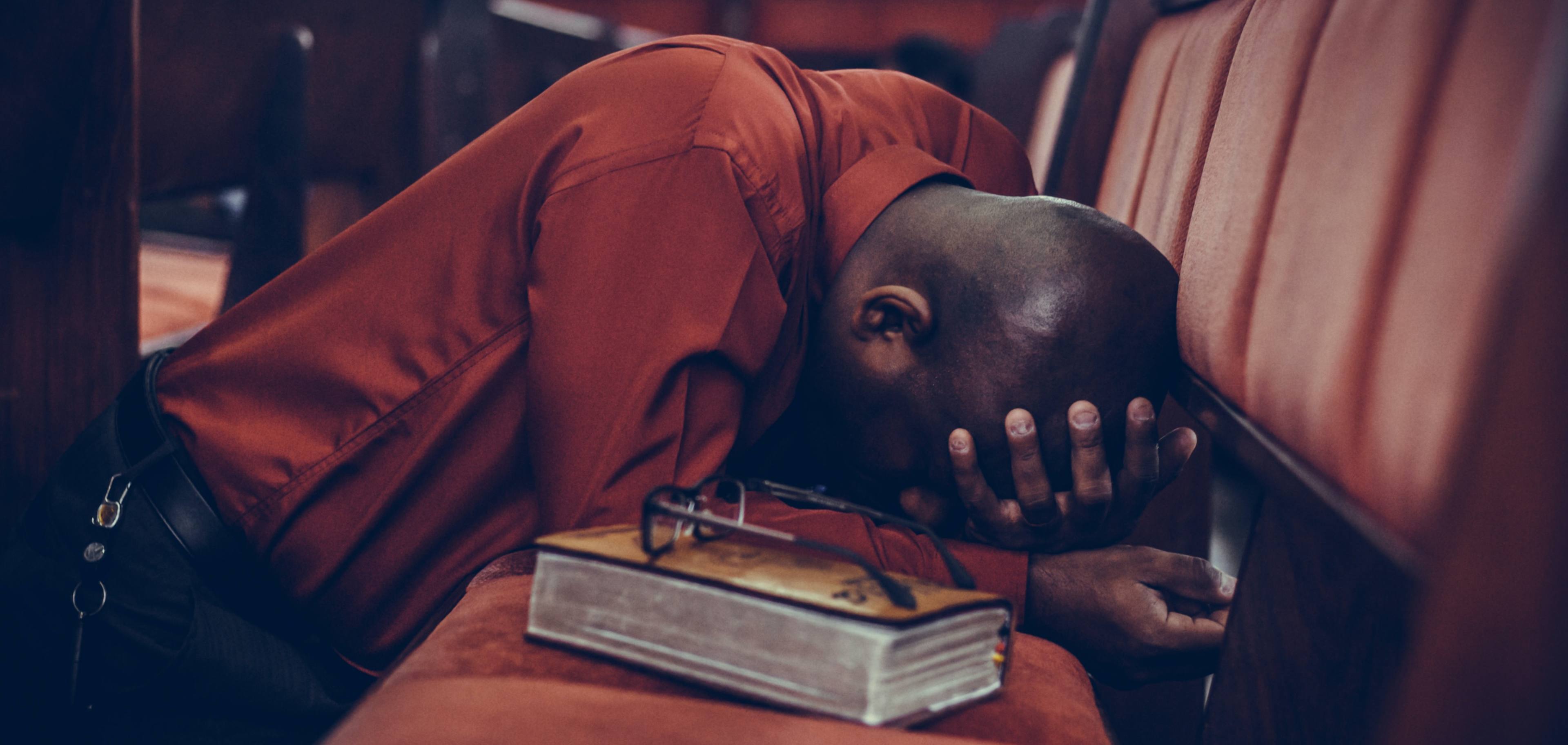 man kneeling praying in a church pew
