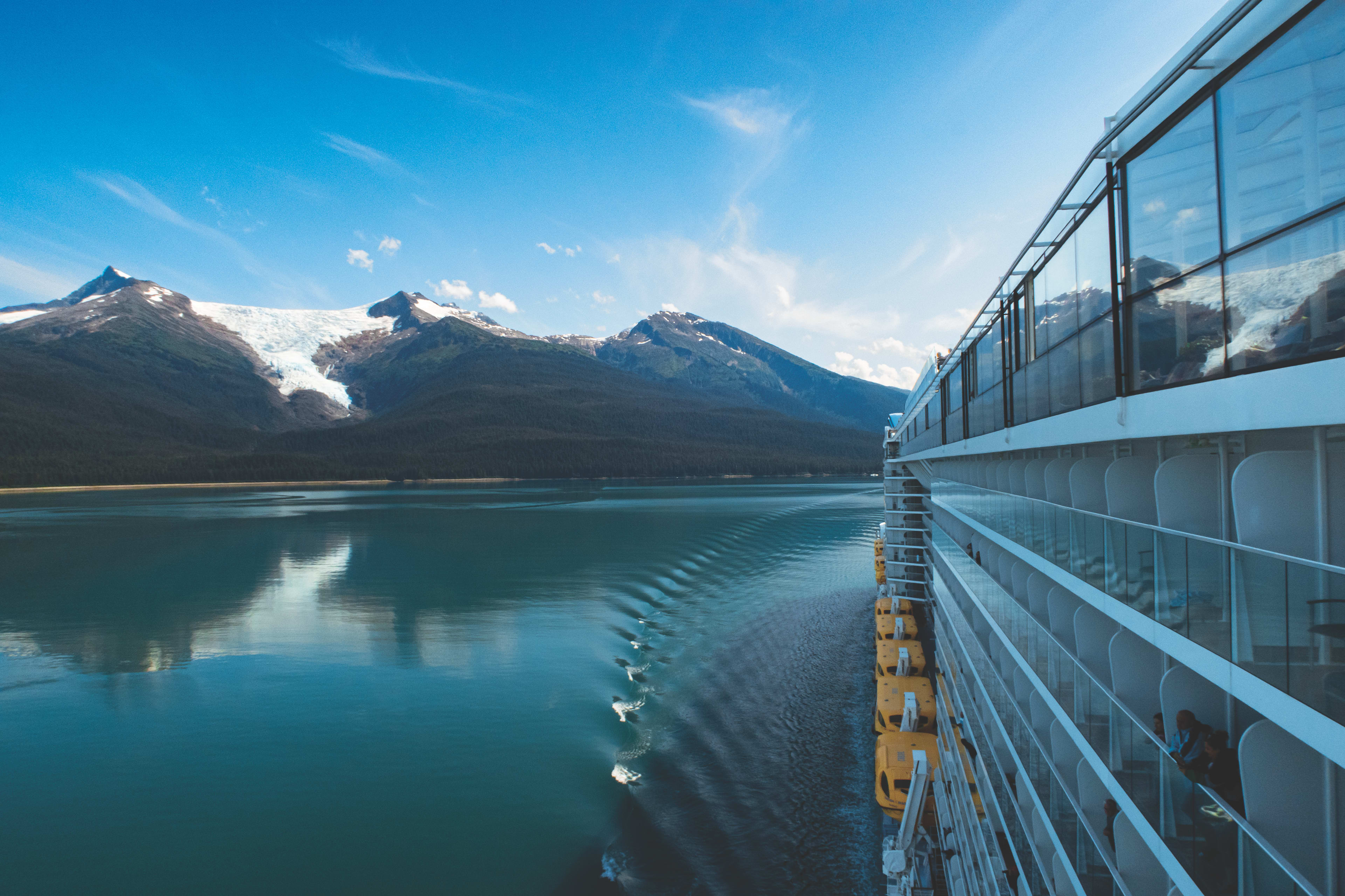 Side of a cruise ship in smooth waters looking at snow capped mountains