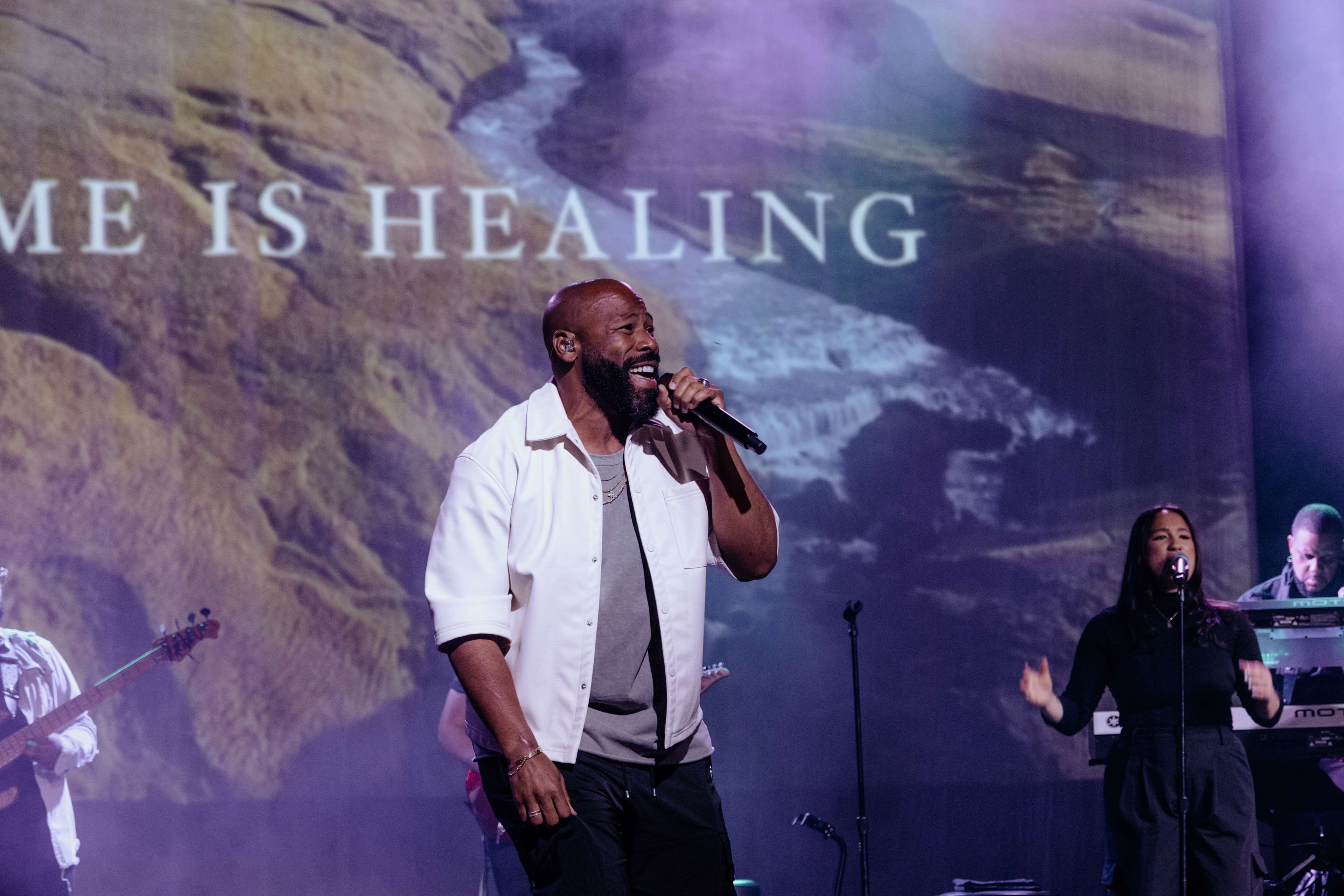 Anthony Evans on stage in front of a large screen with the text "Home Is Healing" displayed behind him
