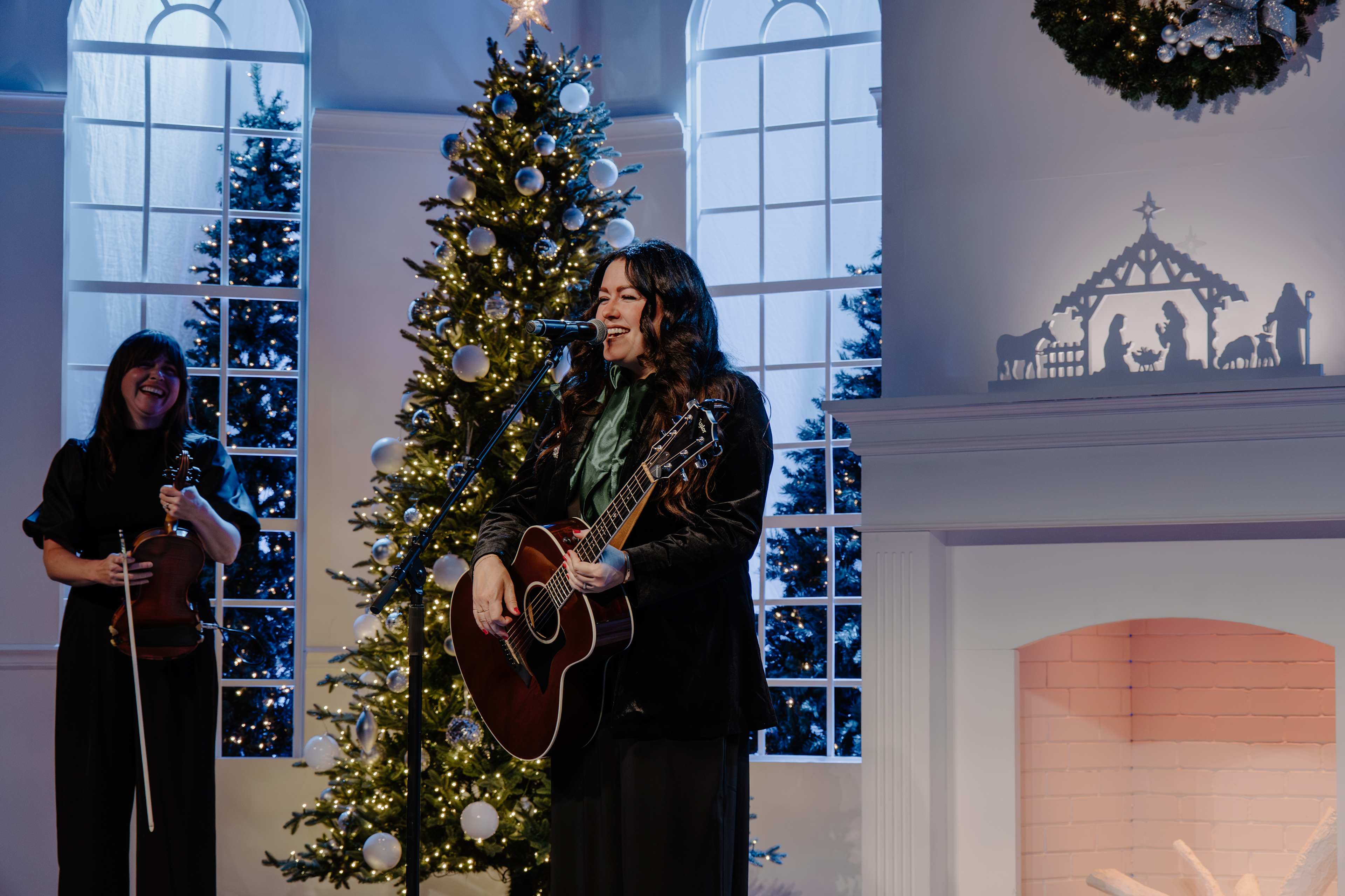 Woman playing guitar and singing in front of Christmas tree