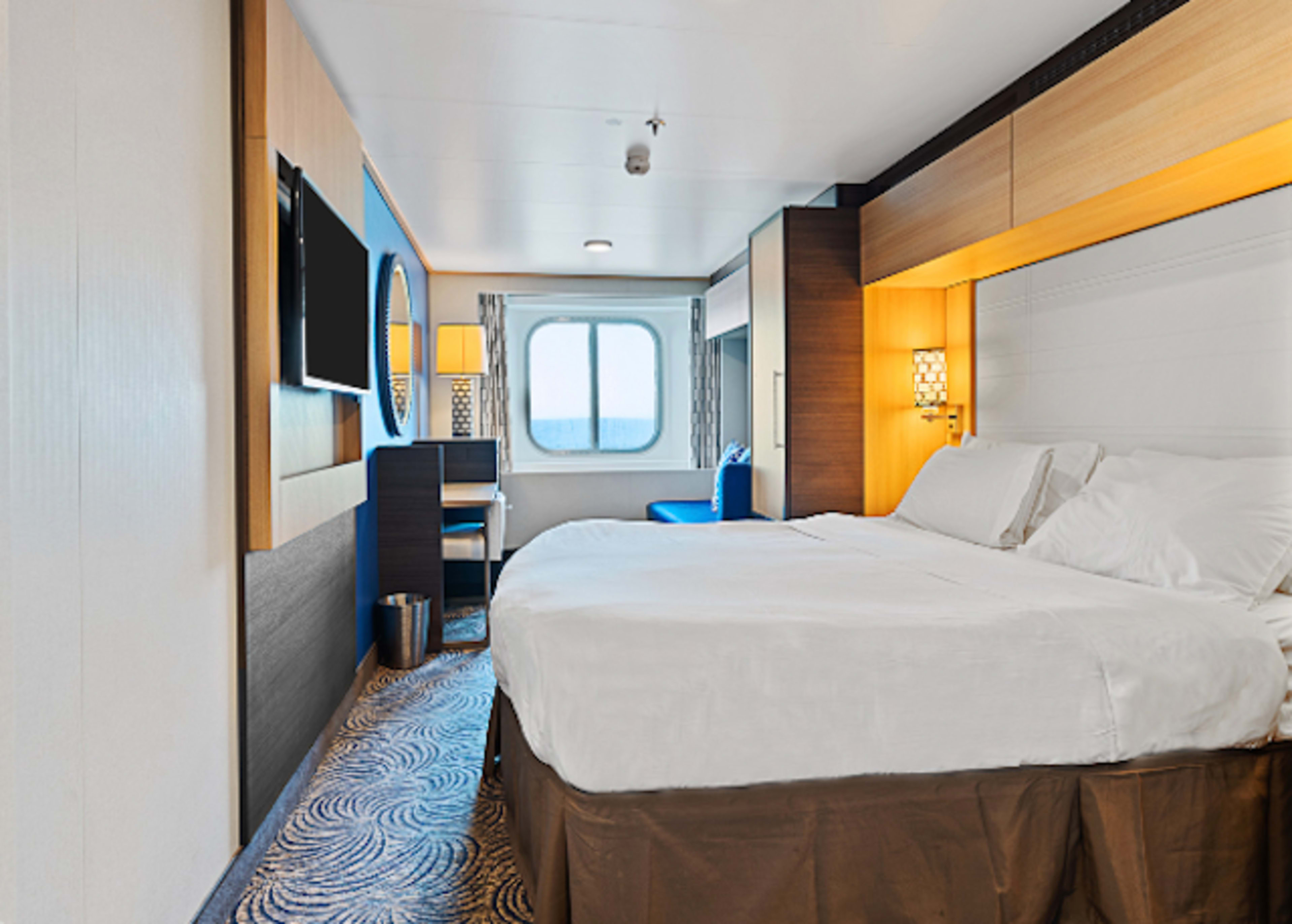 Cruise stateroom with bed, desk, and window in back