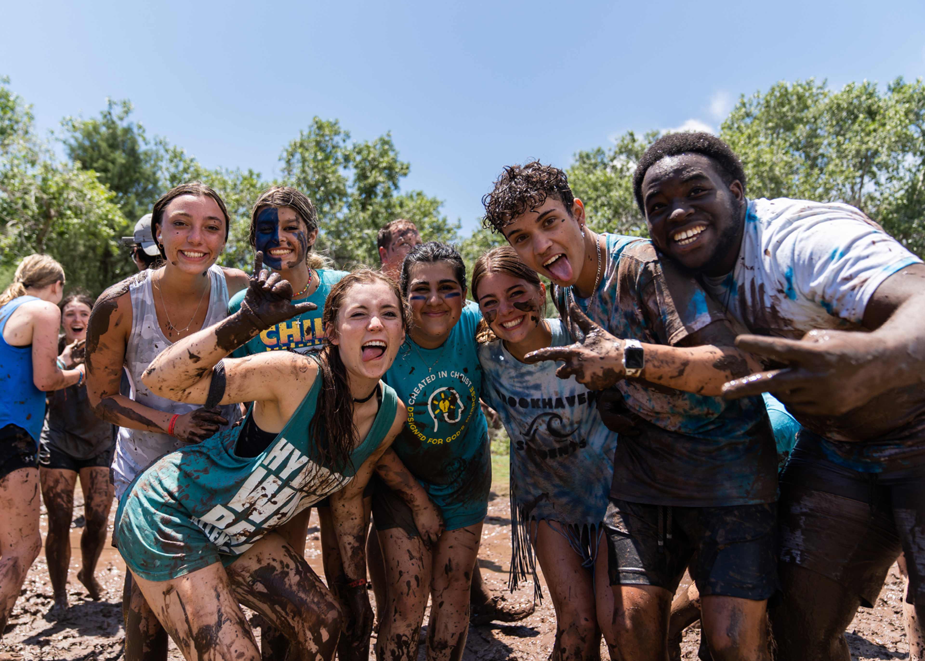 Group of young people smiling and covered in mud during an outdoor team-building activity on a sunny day