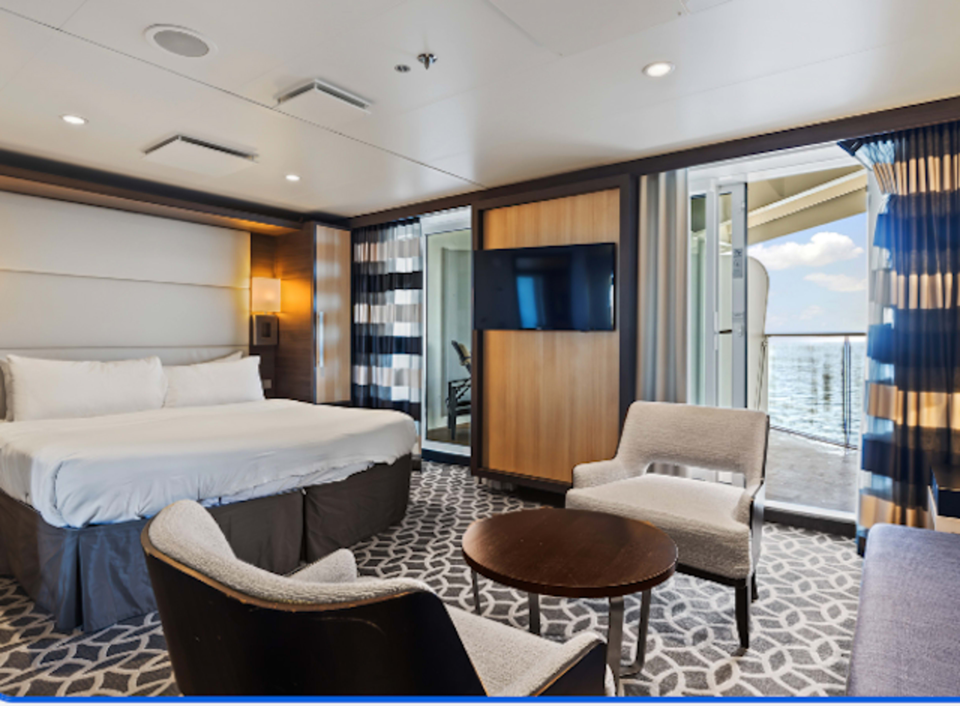 Cruise stateroom suite with bed, table and chairs, and doors to balcony