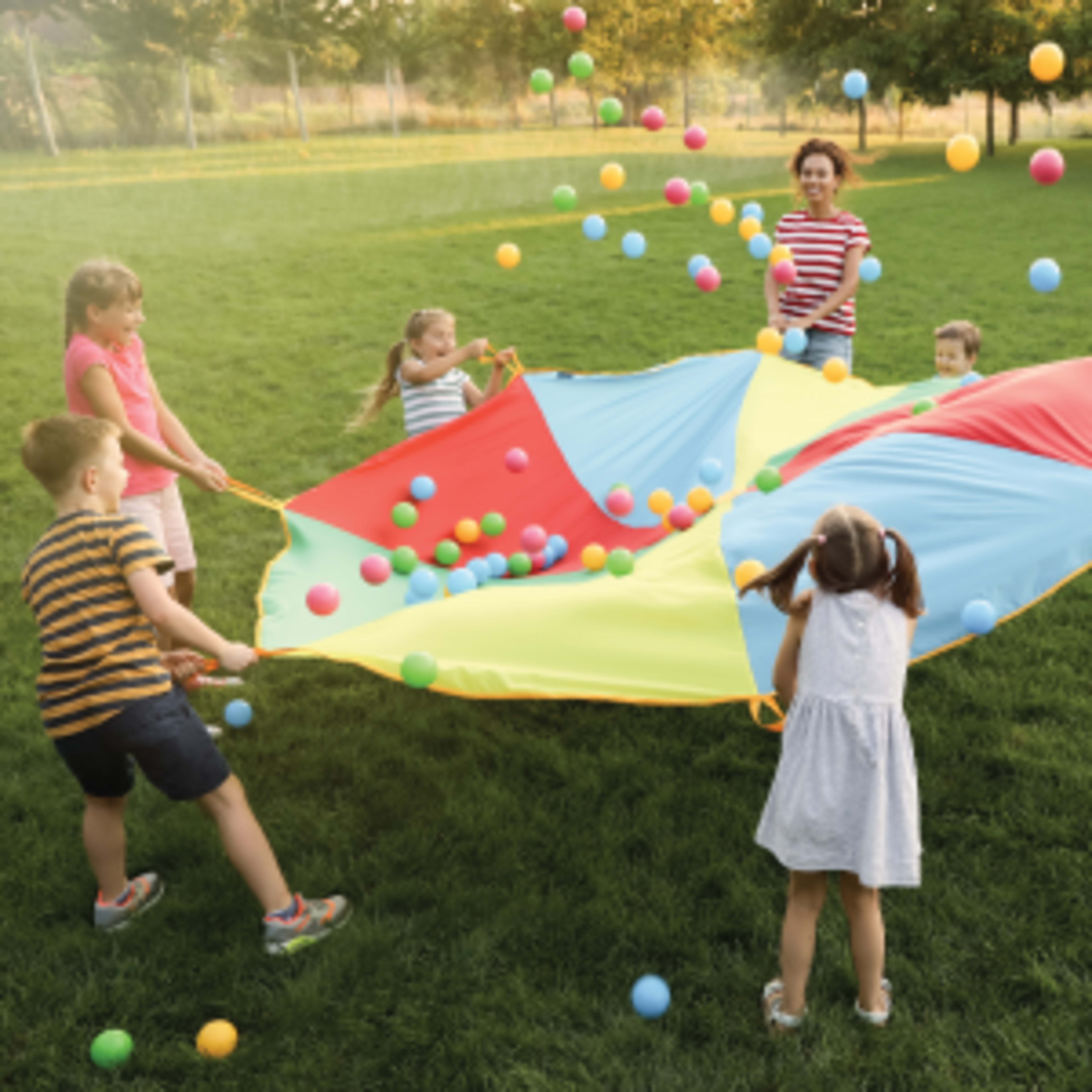 Children playing outdoors with a colorful parachute and bouncing balls on a grassy field