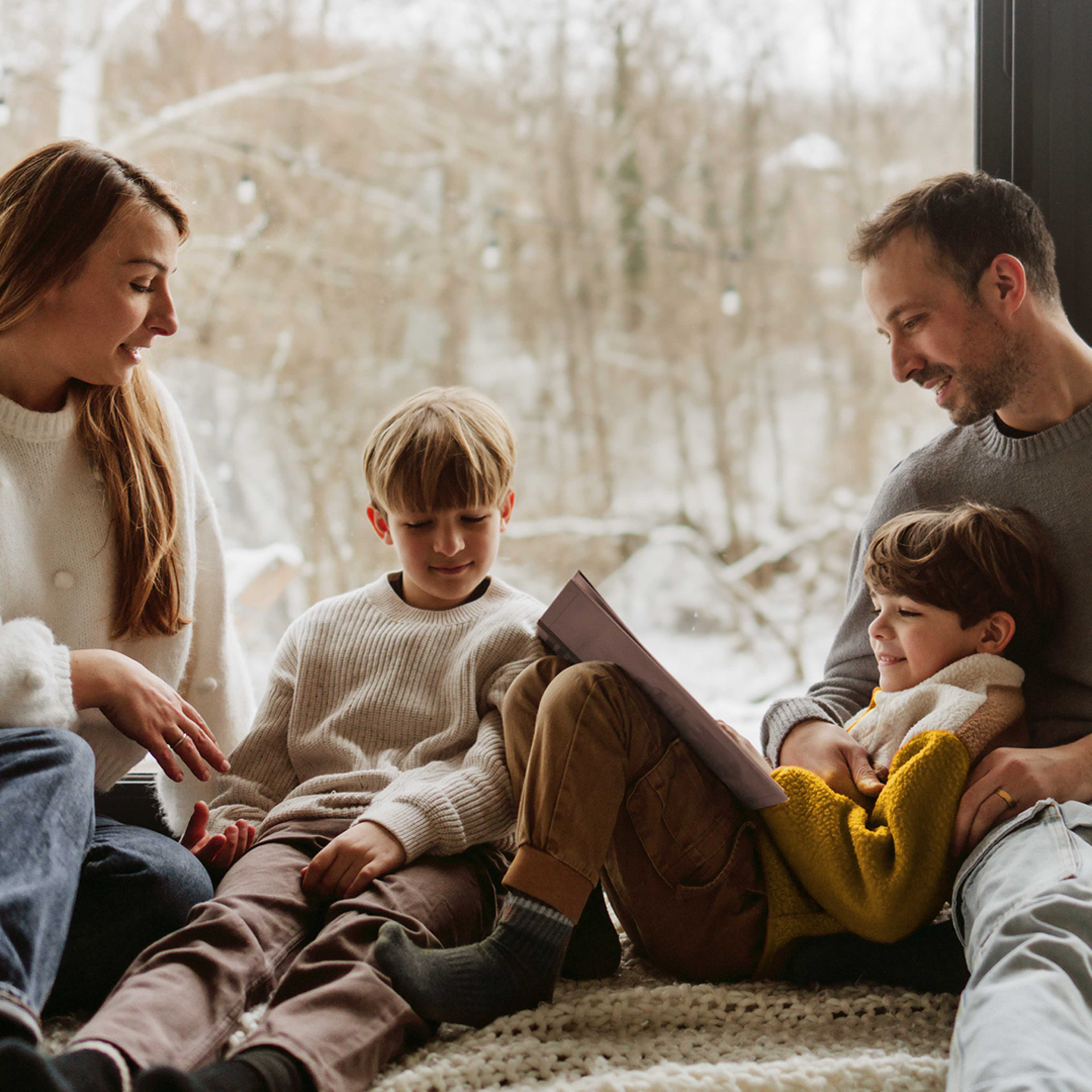 Family sitting by window reading with snow in background