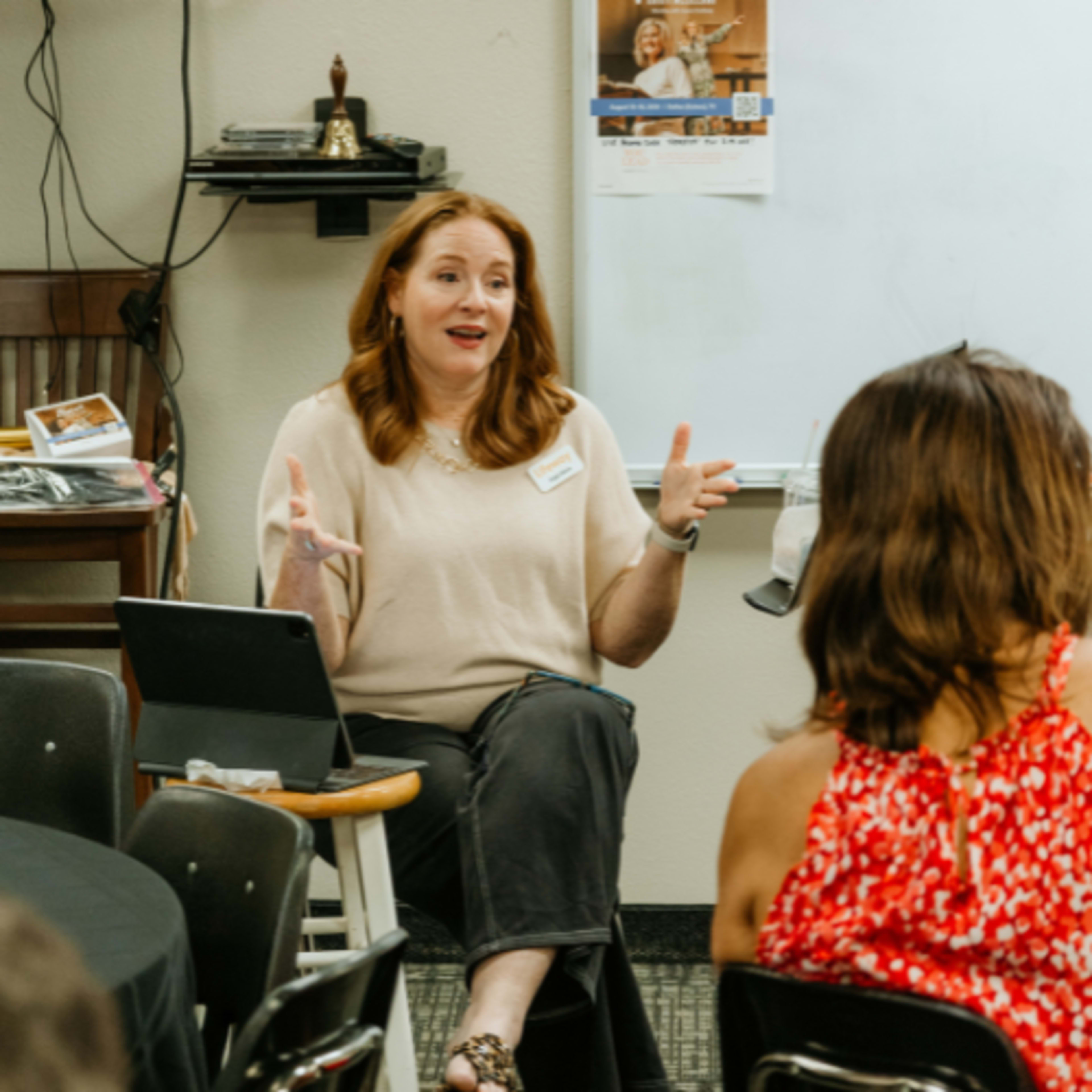 Woman with arms raised speaking while sitting on stool