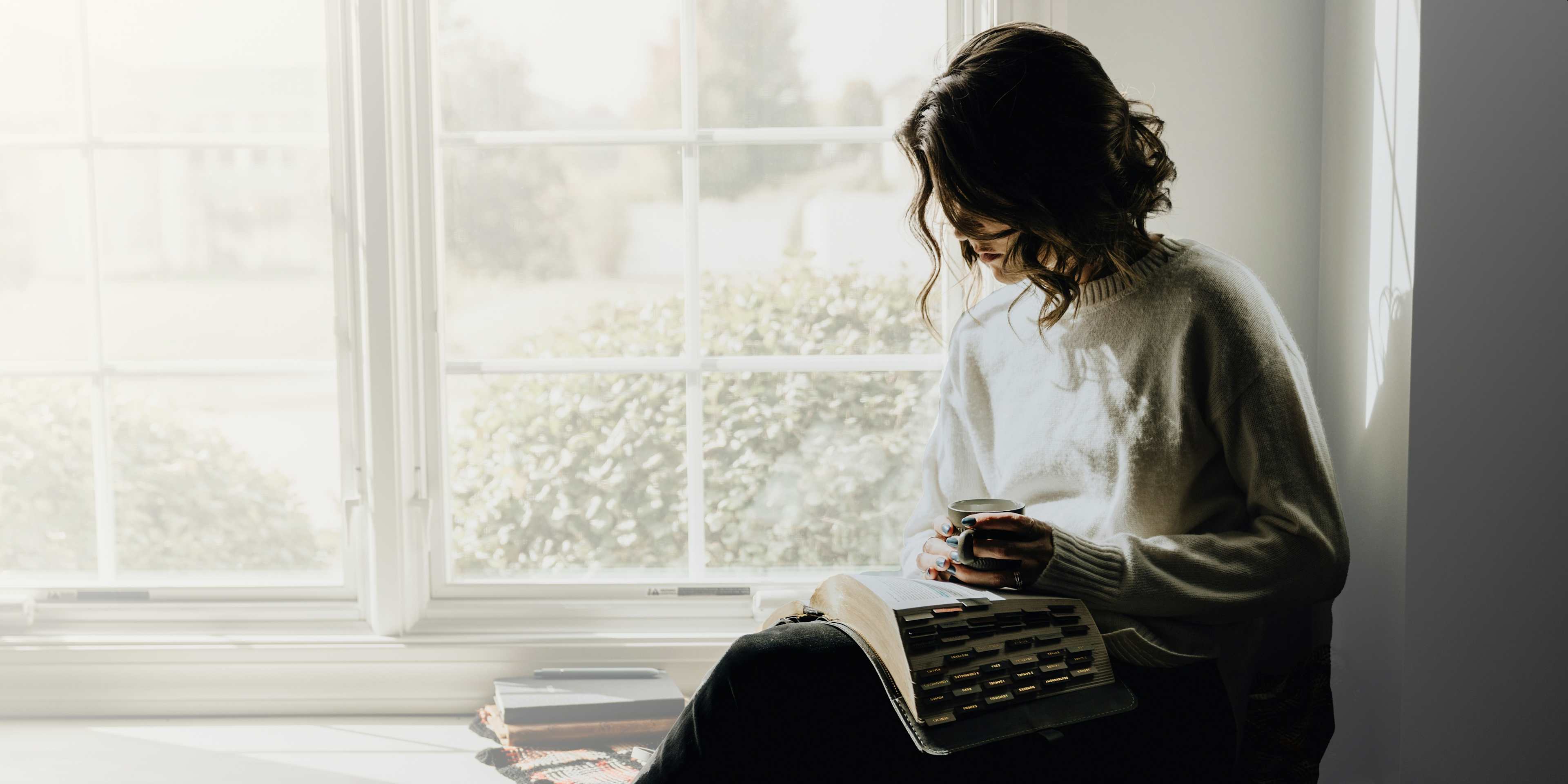 woman sitting beside of a window reading the bible