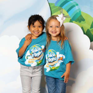 Two girls wearing Take Flight VBS shirts with arms around shoulders
