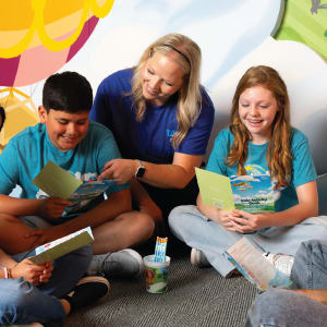 VBS leader sitting on floor with kids reading devotional books