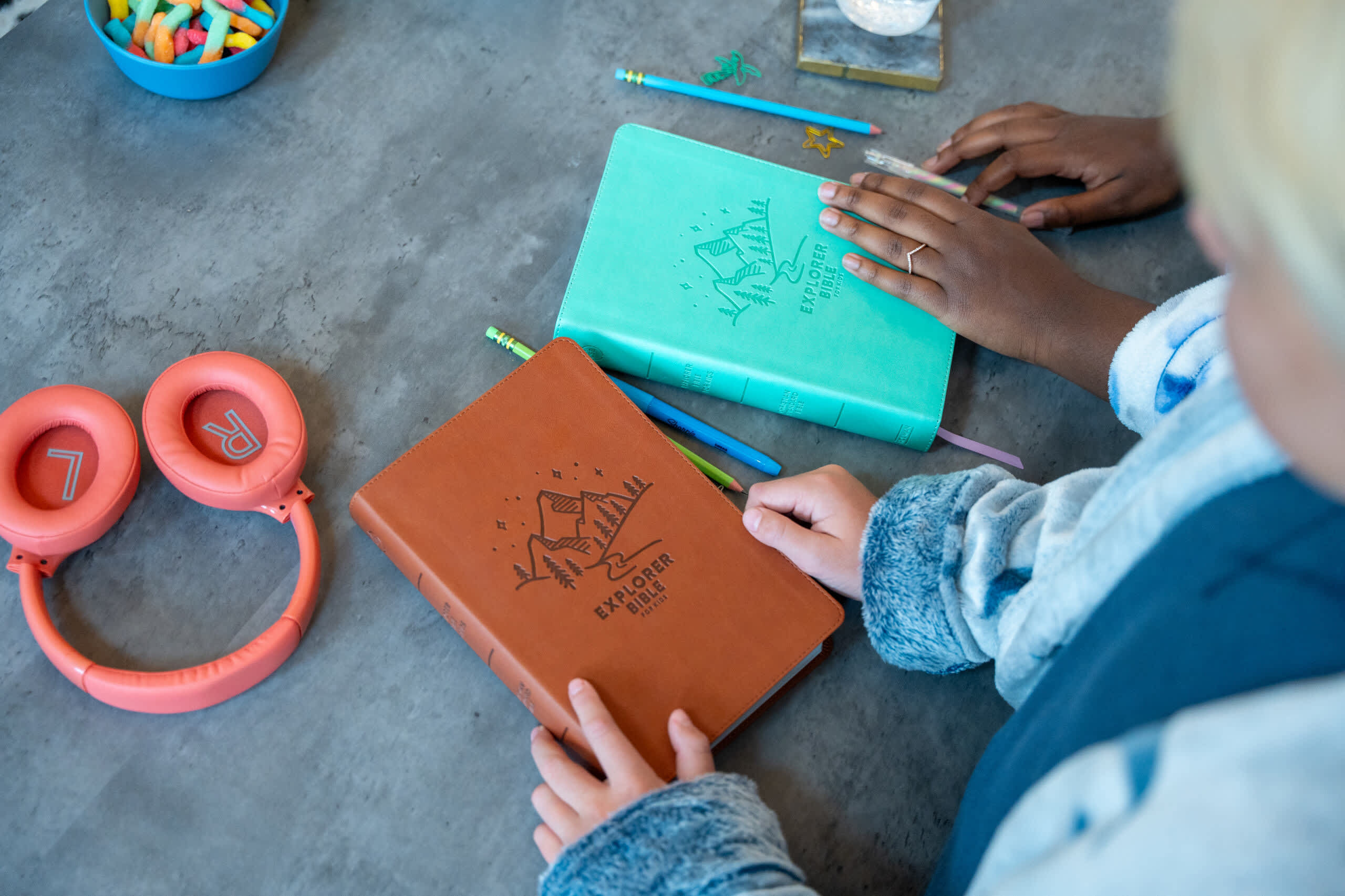 two boys with a brown bible and a teal bible with orange headphones on a desk