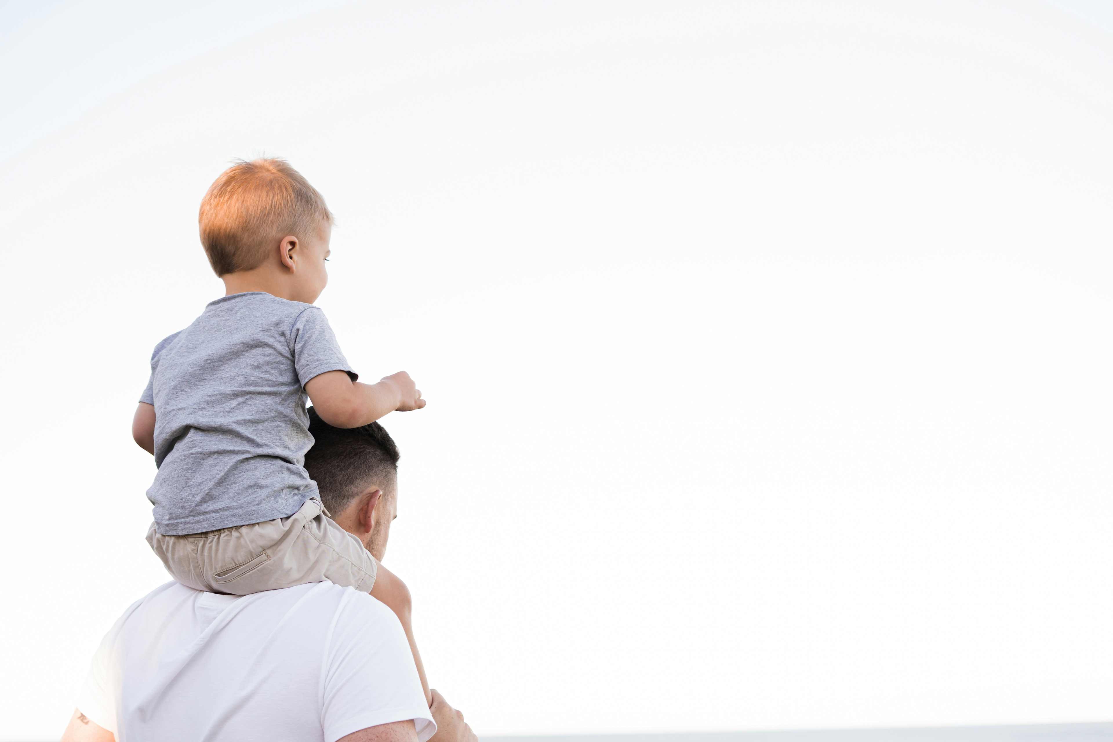 father with toddler son on his shoulders with white background