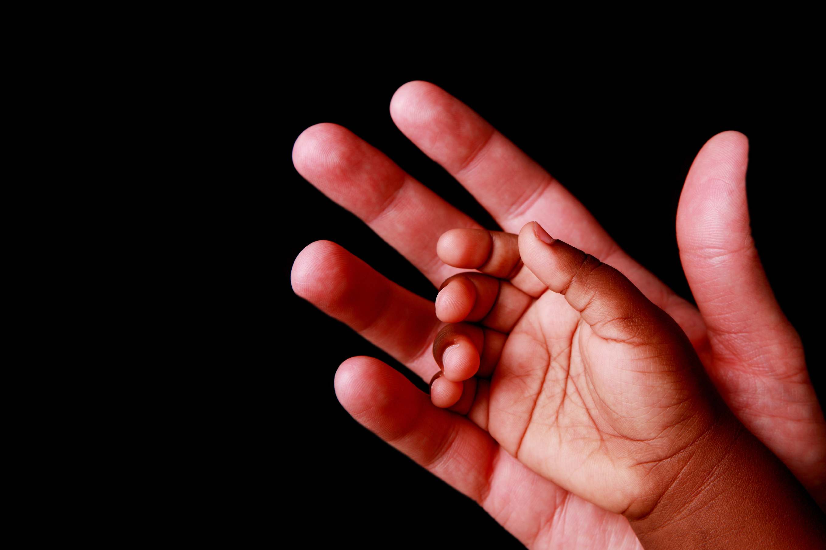 Adult hand and baby hand, adoption photo.