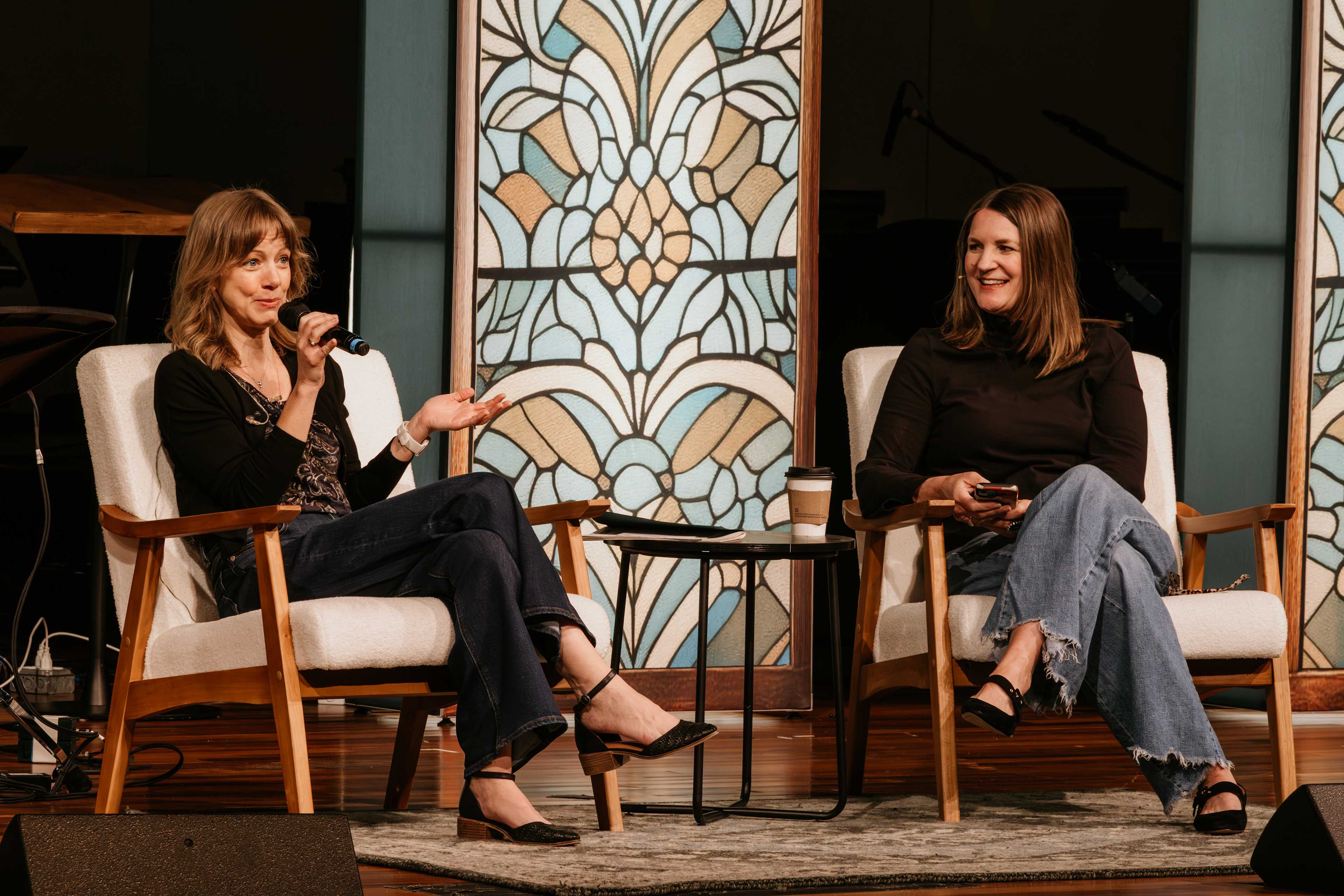 Jen Wilkin and Sandra McCracken sitting on chairs on a stage