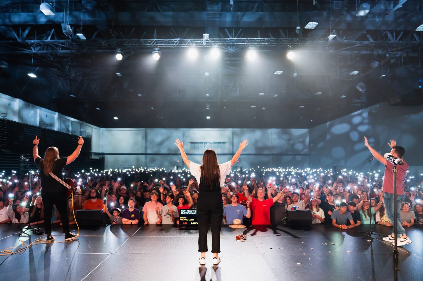 Singers on stage with arms raised in front of large audience